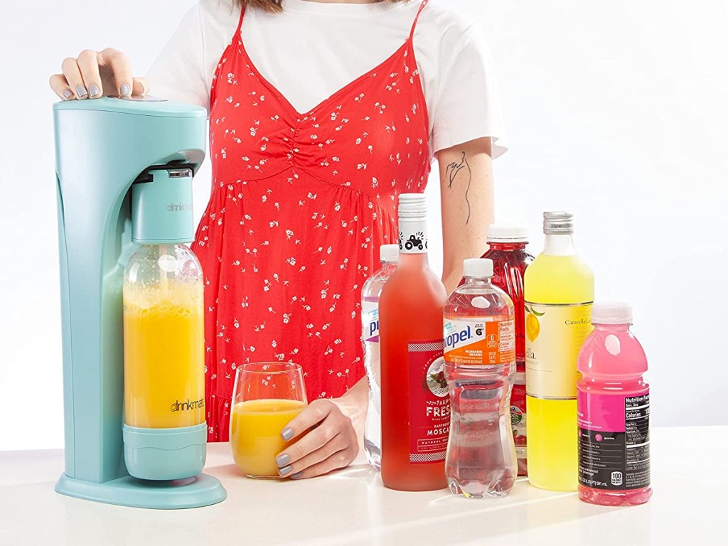 women carbonating orange juice with multiple bottles of drinks near her
