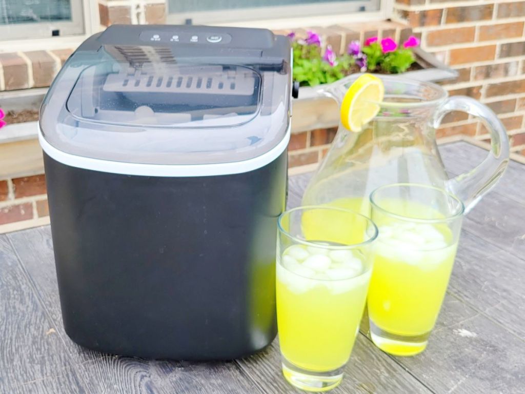 Free Village Ice Maker in Black next to a pitcher and two glasses filled with a yellow liquid