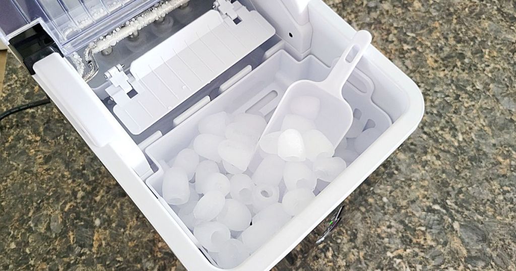 Portable Countertop Ice Maker filled with ice and scoop laying in bin