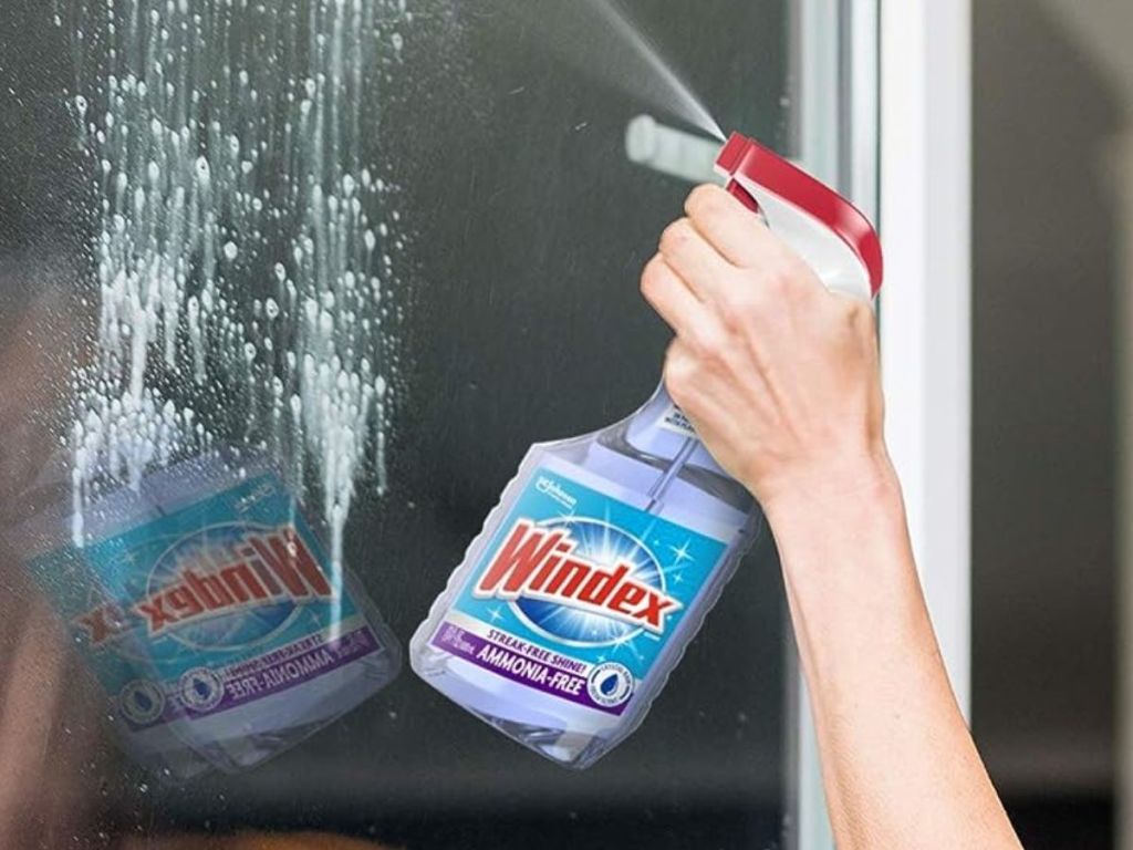 hand spraying a bottle of Windex Ammonia-Free Glass Cleaner Spray onto a window