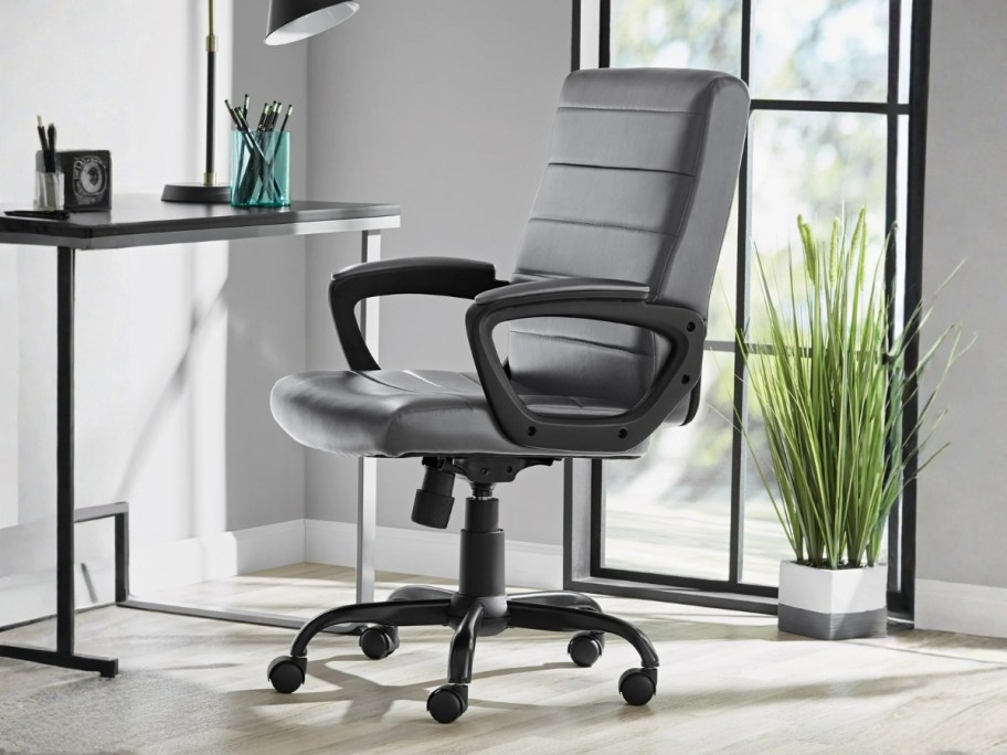 a black bonded leather office chair with wheels by a desk
