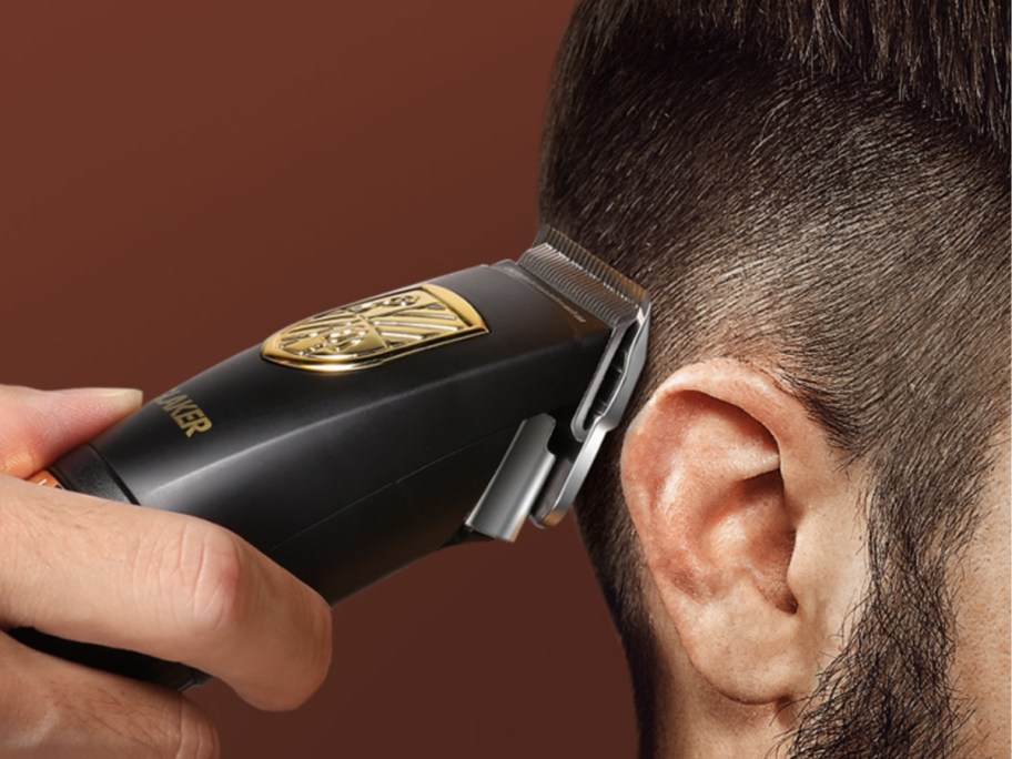 man using a black and gold hair trimmer to freshen up his fade