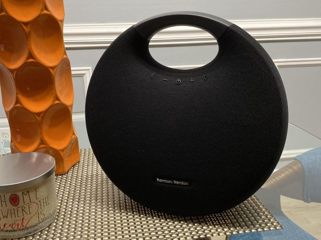 Solid black speaker sitting on a table by a vase and candle