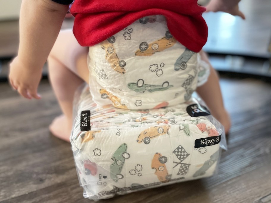 boy in diaper sitting on pack of diapers