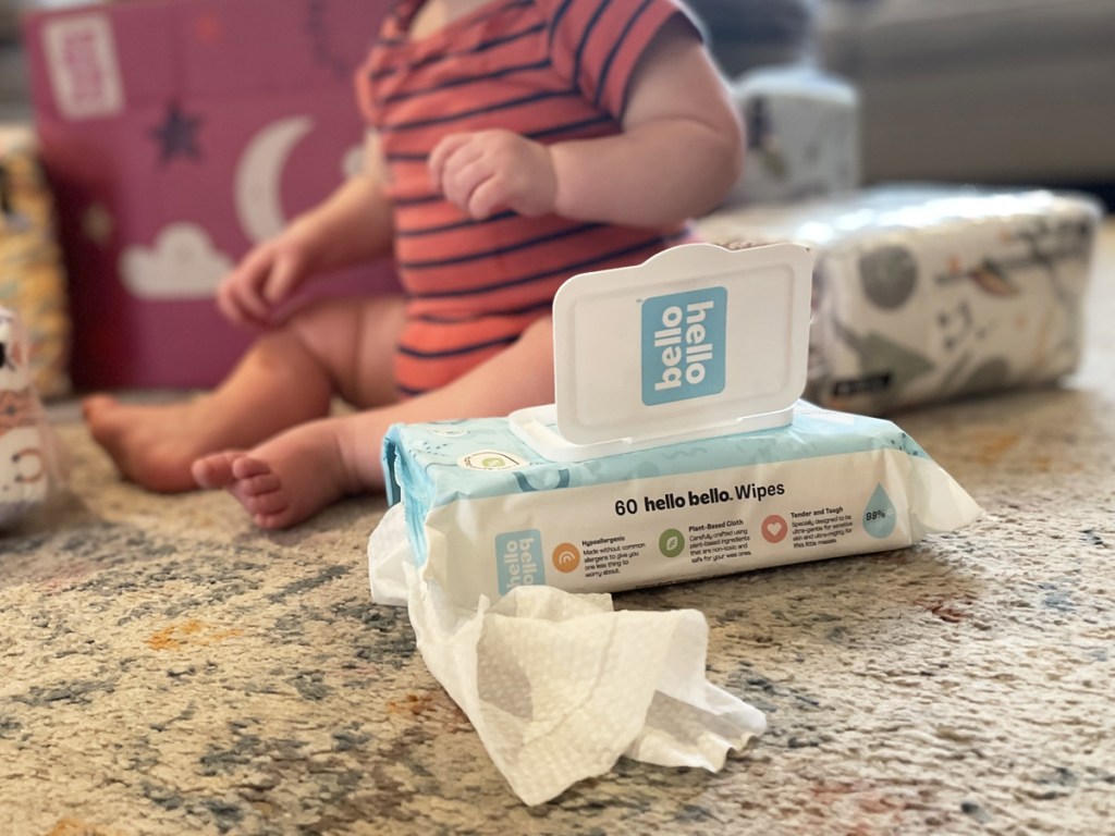 baby sitting on floor next to pack of hello bello wipes