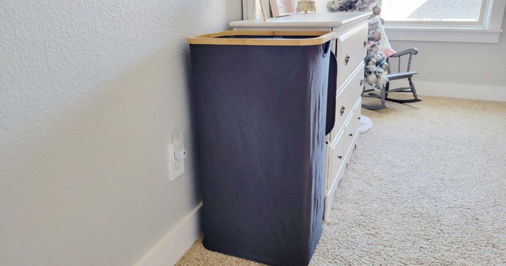 dark gray laundry hamper with bamboo lid base opened in bedroom next to white dresser