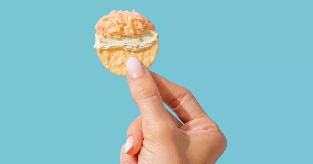 woman holding up a cracker with cream cheese and salmon