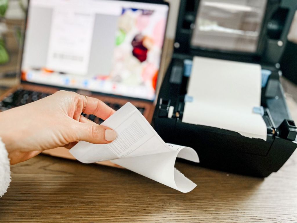 hand peeling a shipping label off the backing in front of a thermal printer