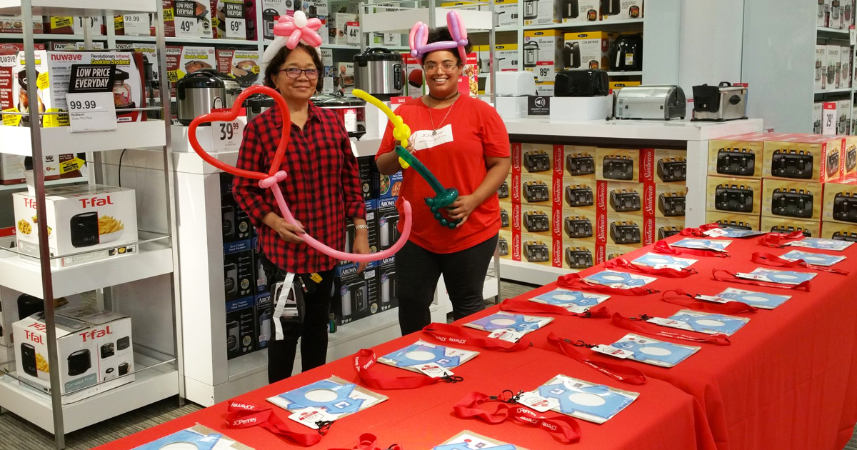 two women with balloon animals in front of red tables with kids crafts
