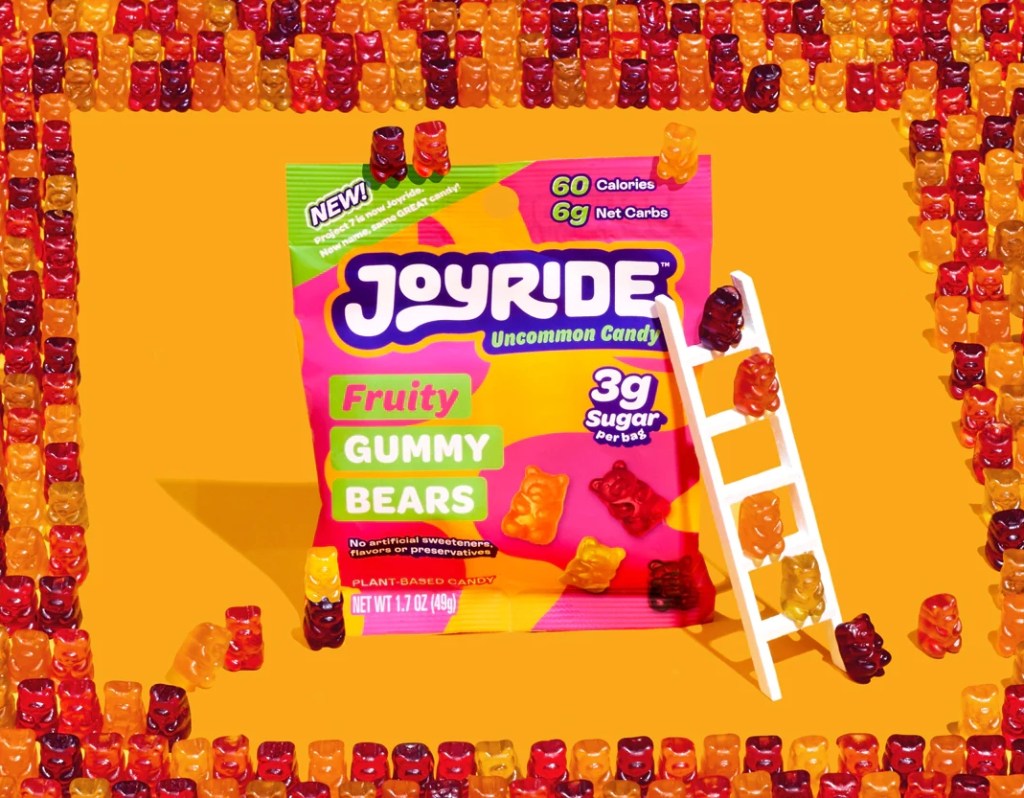 Bag of Joyride Gummy bears surrounded by gummy bears with a ladder on the bag and gummy bears climbing up