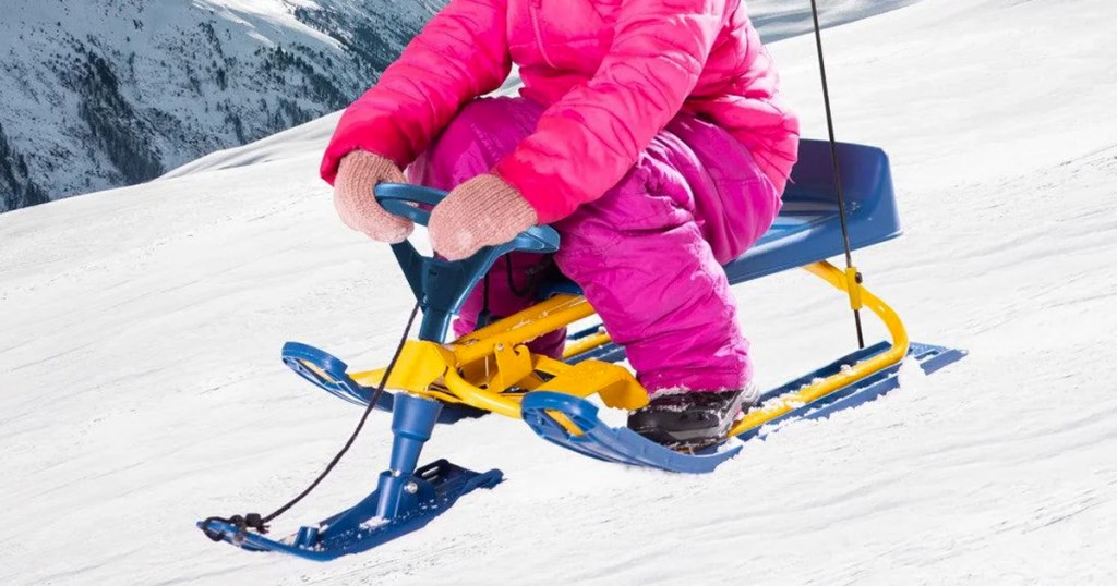 girl riding on yellow and blue snow sled