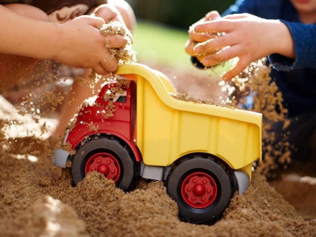 Kids playing with a Green Toys Dump Truck in sand