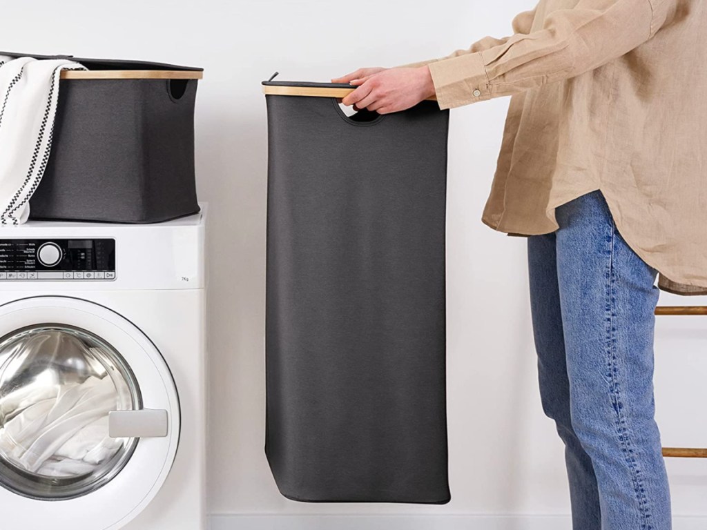 woman holding gray colored collapsible laundry basket next to dryer
