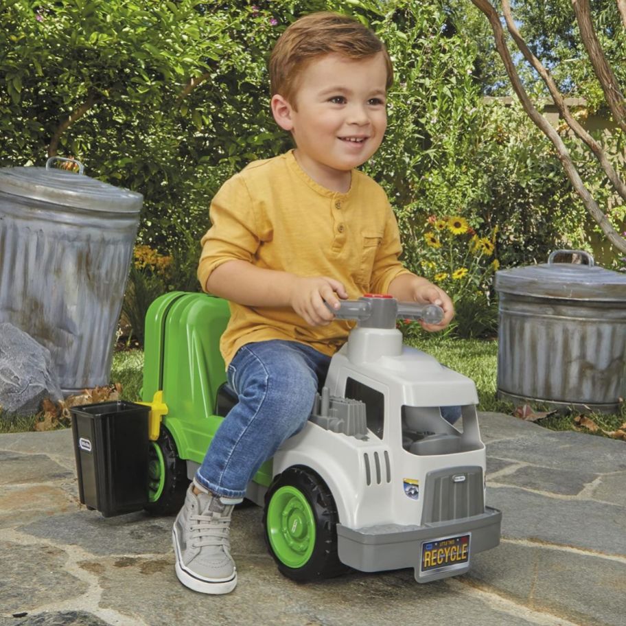 a toddler boy riding on a little tikes garbage truck