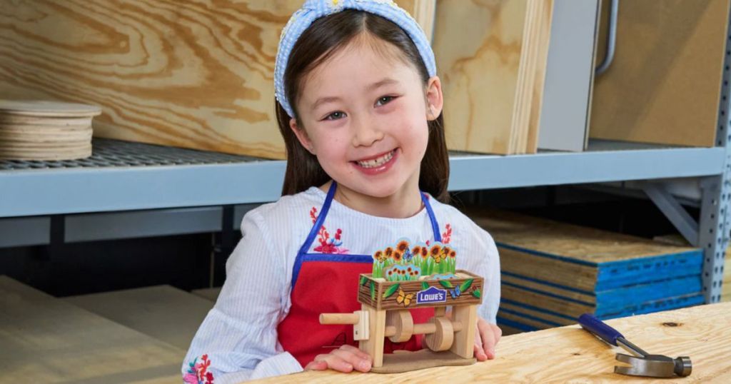 Little girl wearing a Lowe's apron with a DIY wooden flower box in front of her on a table