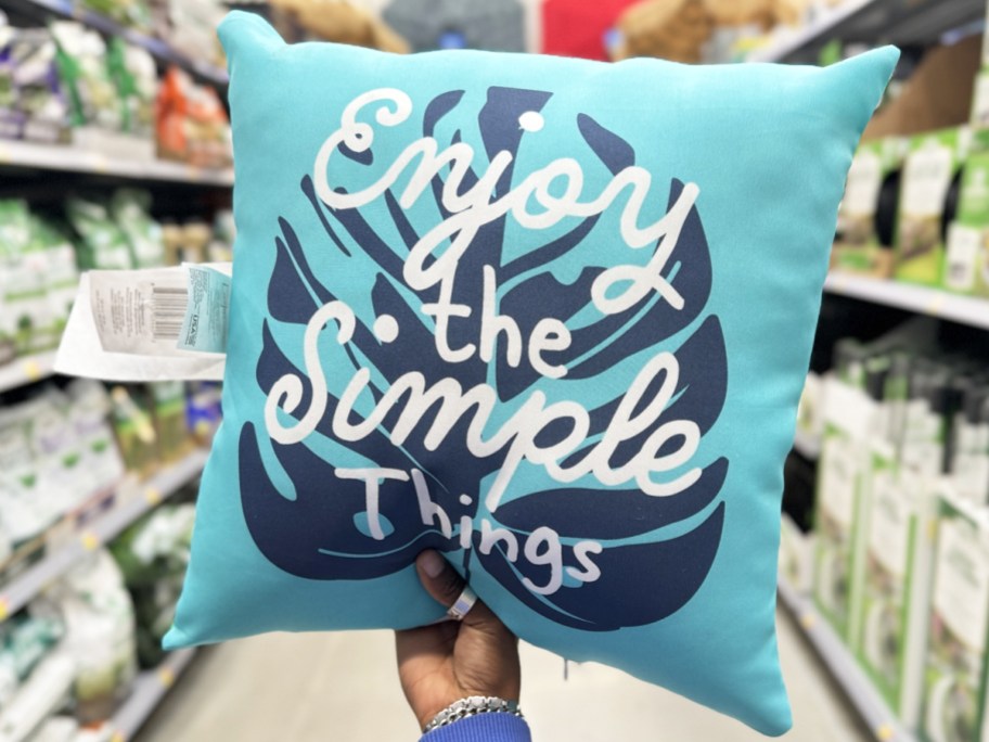 hand holding up a blue throw pillow that says "enjoy the simple things"