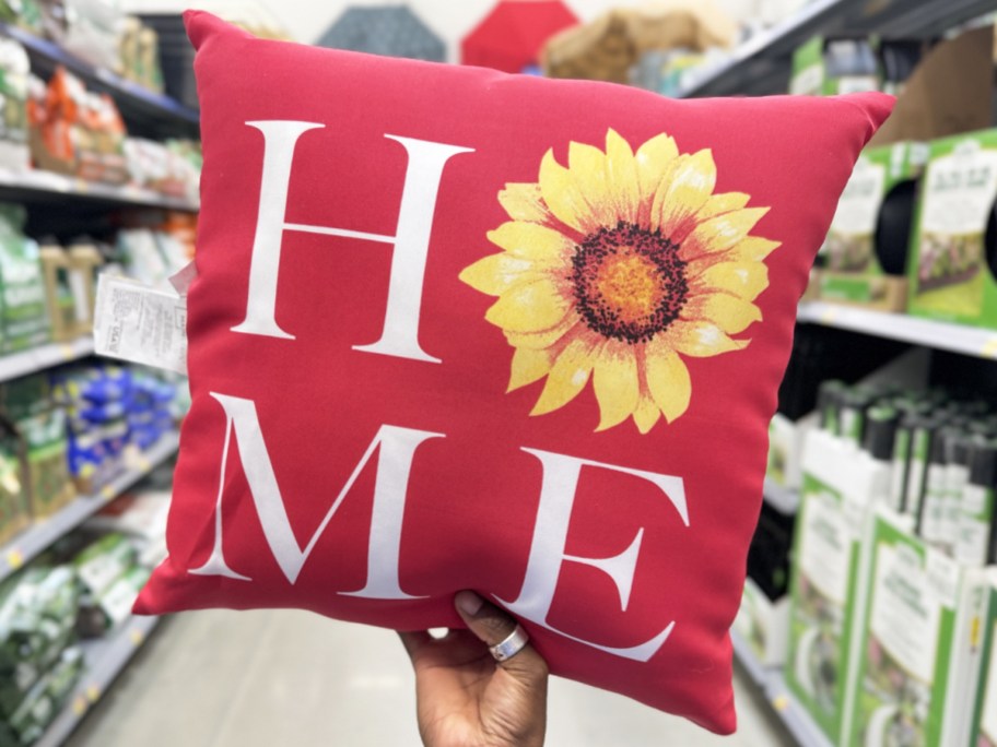 hand holding a red throw pillow that says HOME with a sunflower in place of the letter O