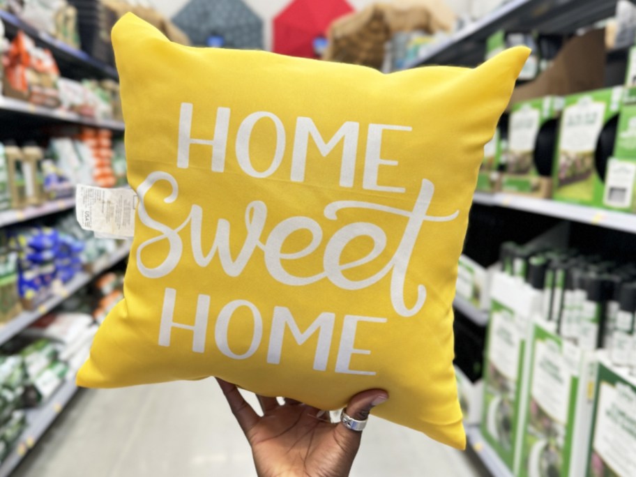 hand holding a yellow throw pillow that says "home sweet home"