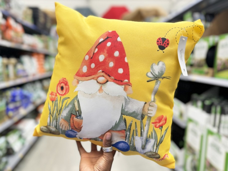 hand holding a yellow throw pillow with a garden gnome on it