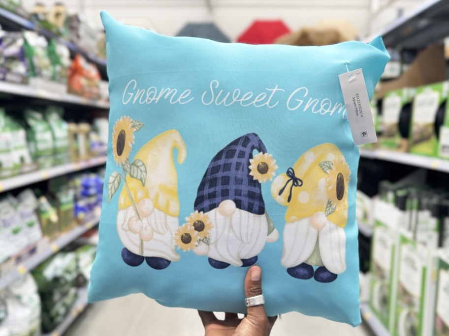 hand holding up a blue throw pillow with 3 gnomes that says "gnome sweet gnome"