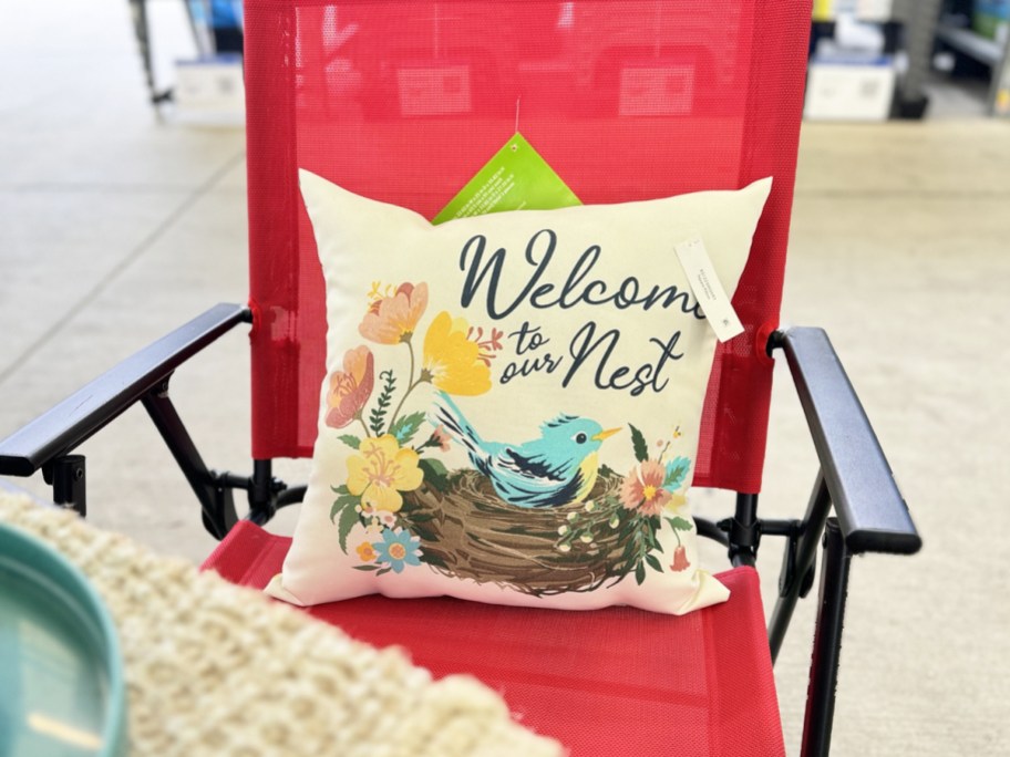 red patio chair with throw pillow that says welcome to our nest