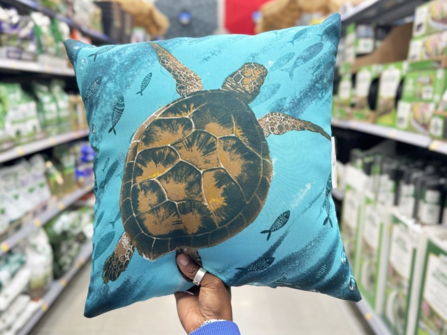 hand holding up a throw pillow with a sea turtle on it