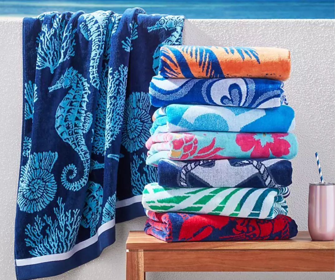 A pile of folded Members mark Beach Towels with one open hanging over a wall to the left of the stack