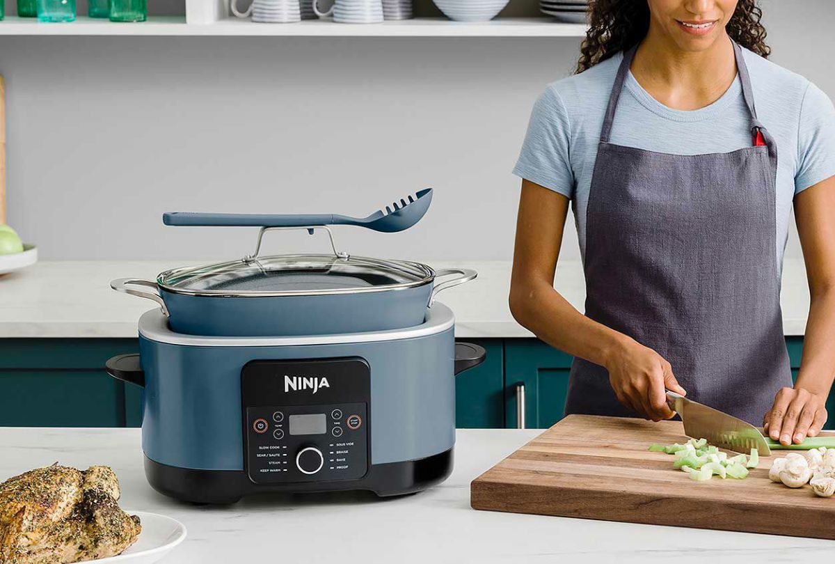 Ninja Foodi PossibleCooker PRO 8.5-Quart on a kitchen counter next to a woman who is chopping vegetables