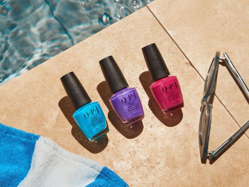 blue purple and pink OPI nail polish bottles lined up on patio by pool