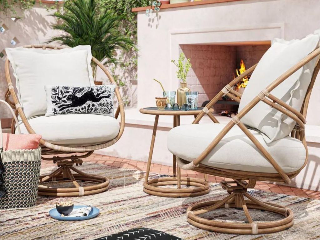 Opalhouse 3 piece patio set with two swivel chairs with cushions and a table on a patio in front of an outdoor fireplace