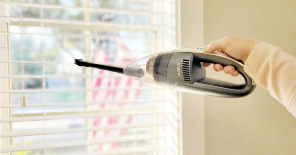 person cleaning the blinds with a handheld vacuum