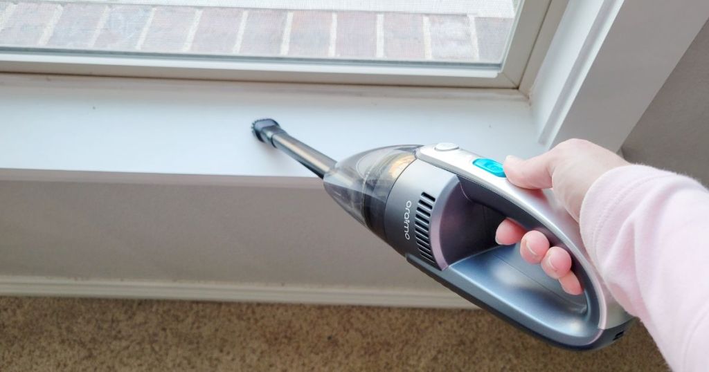 person cleaning the window sill with a handheld vacuum