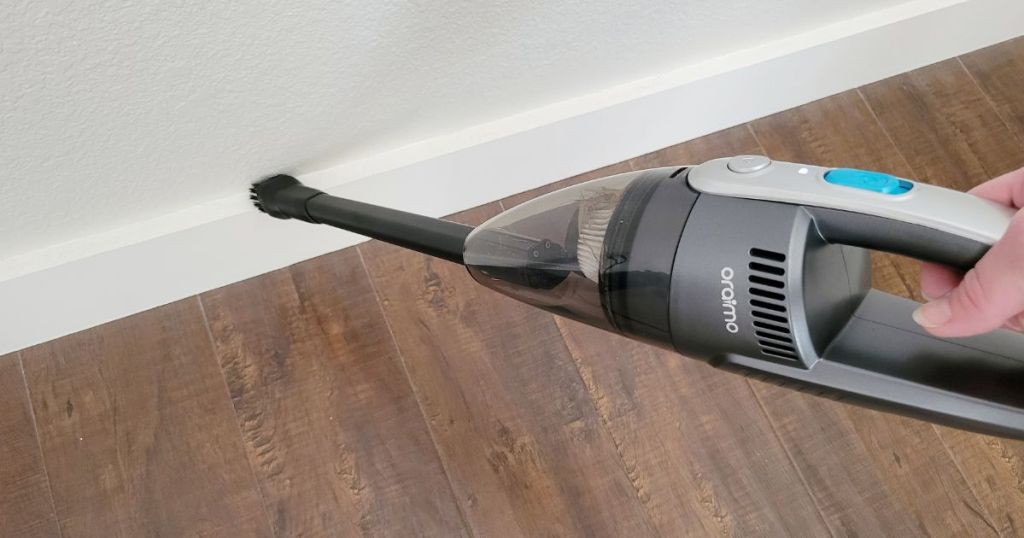 person cleaning the baseboard with a handheld vacuum