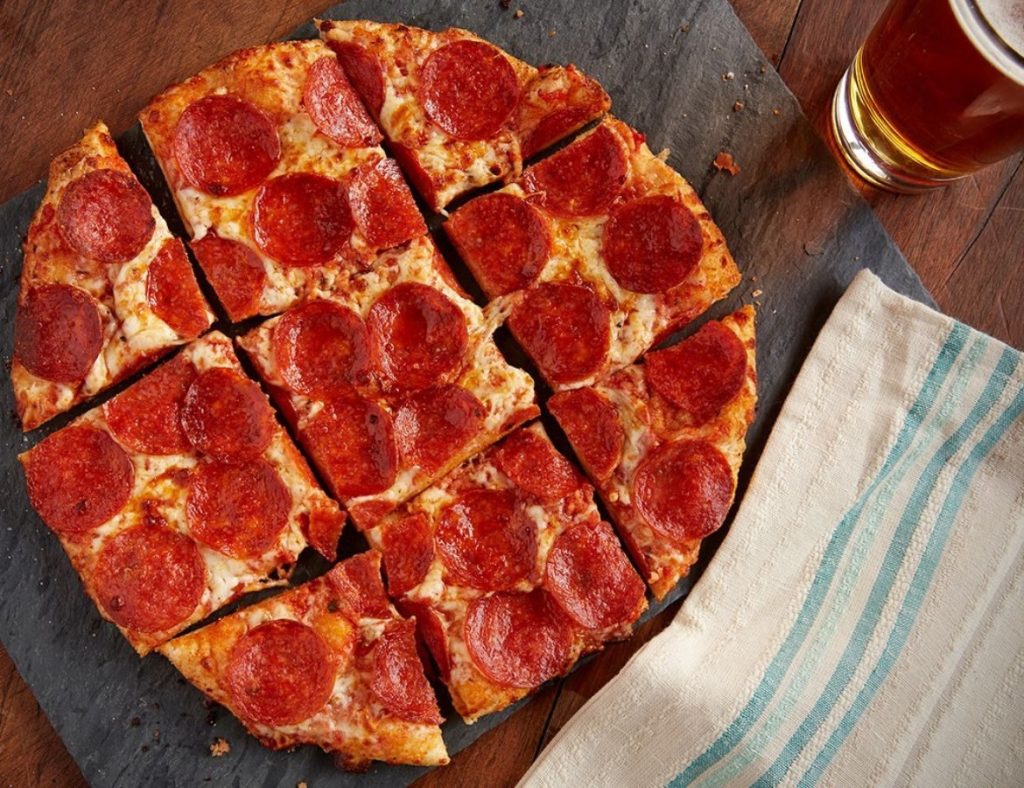 A personal size pepperoni pizza cut into 9 slices sitting next to a pint of beer