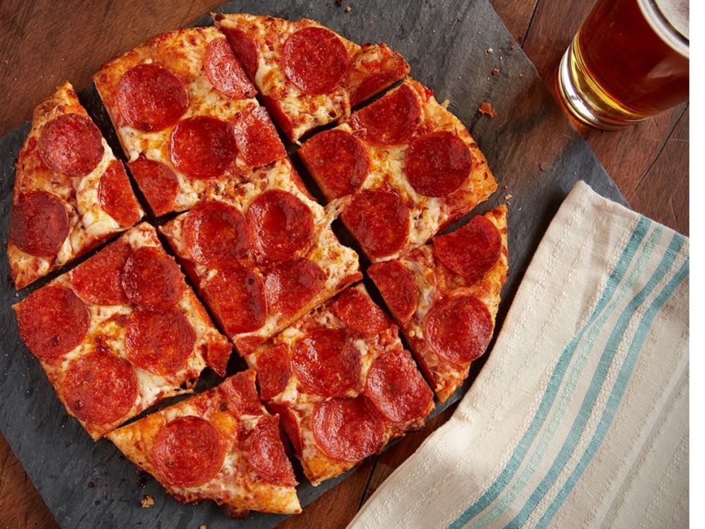 A personal size pepperoni pizza cut into 9 slices sitting next to a pint of beer