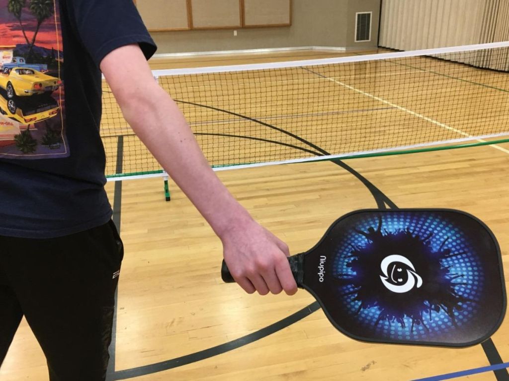 behind view of a kid playing pickleball indoors in front of a net