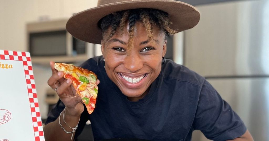 Woman wearing a hat and holding up a slice of Pizza