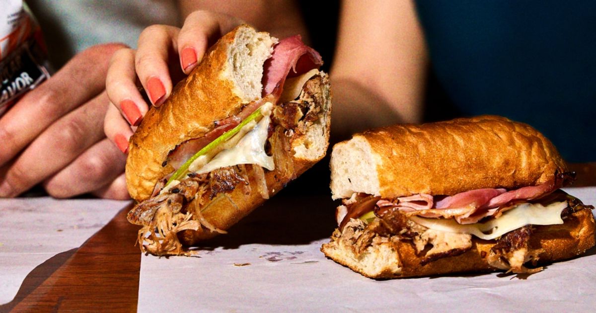 a womans hand holding a Potbelly cubano sandwich which you can get as part of a graduation catering discount from the sandwich shop