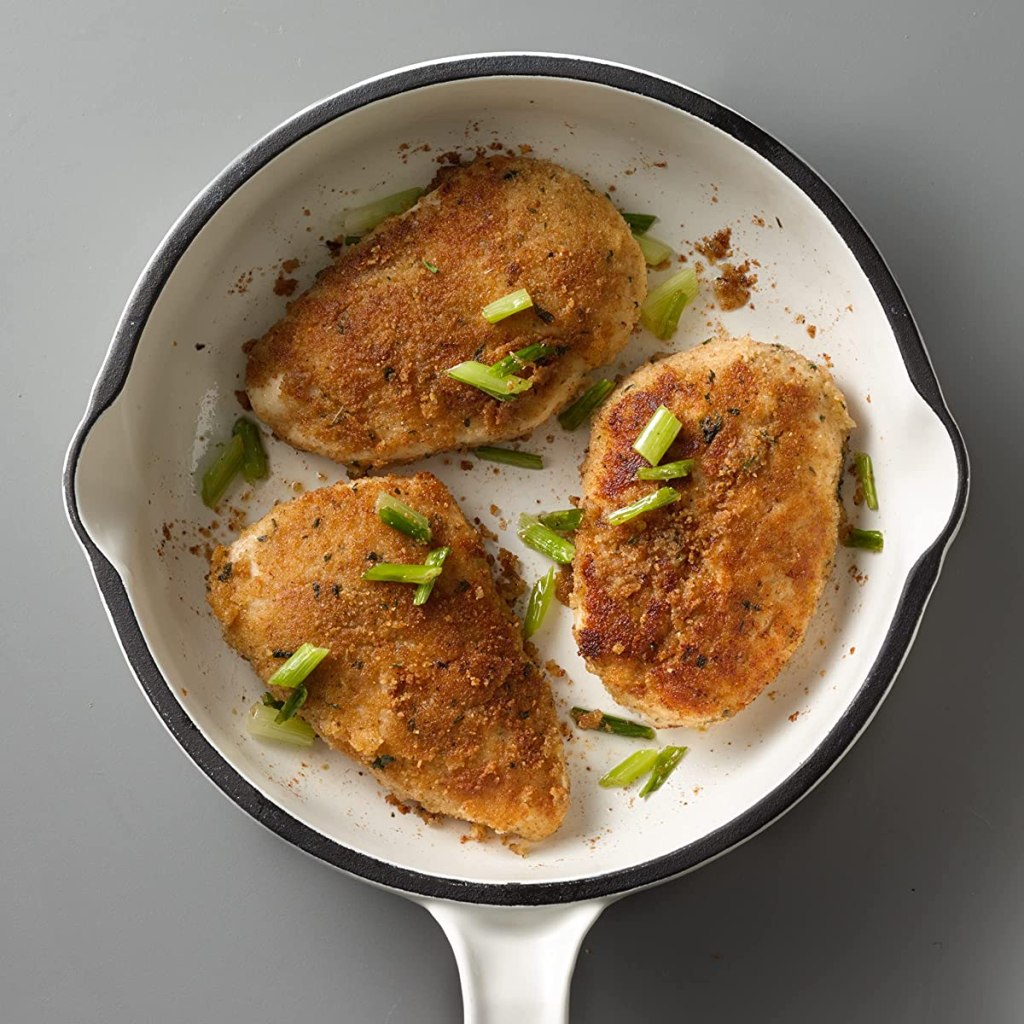 Three pieces of chicken in a white pan with bread crumbs on top