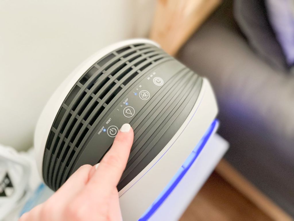 Hand pushing a button on the top of an air purifier