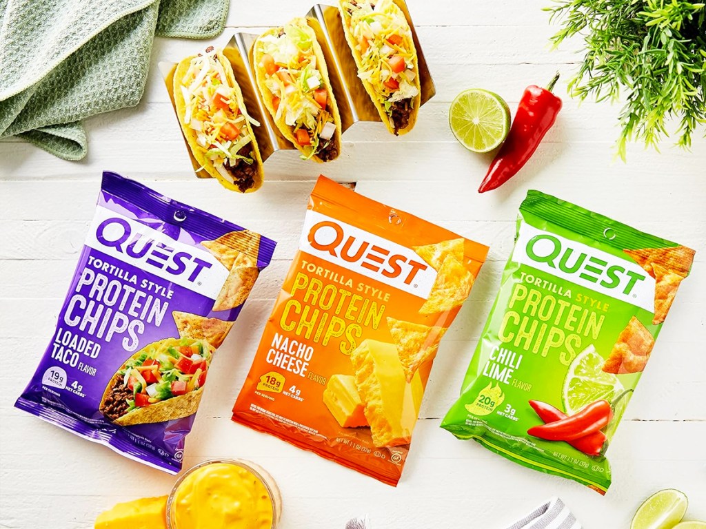 purple, orange, and green bags of Quest Nutrition Tortilla Style Protein Chips on table near tacos