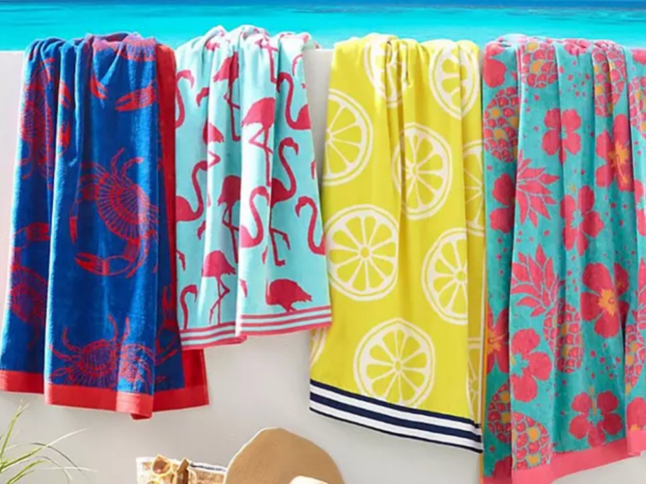 Different color, oversize beach towels, draped over white wall in front of ocean