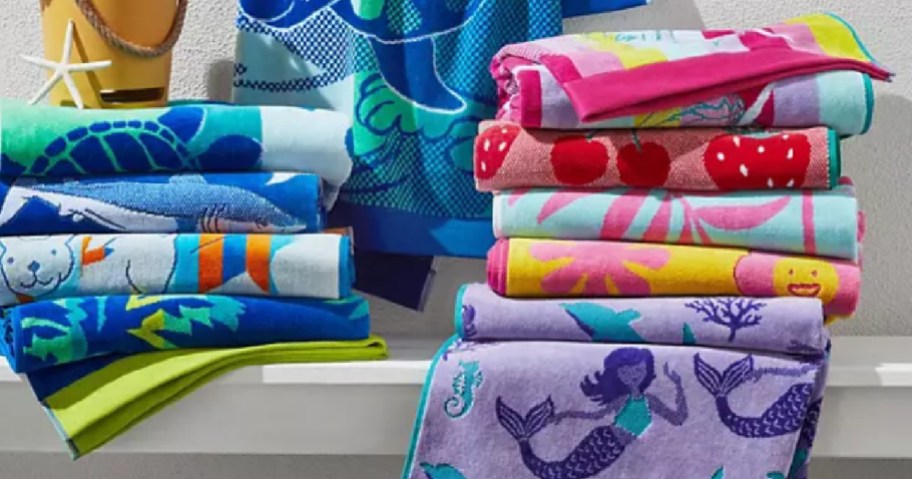 Stack of colorful kids themed beach towels outside by white fence