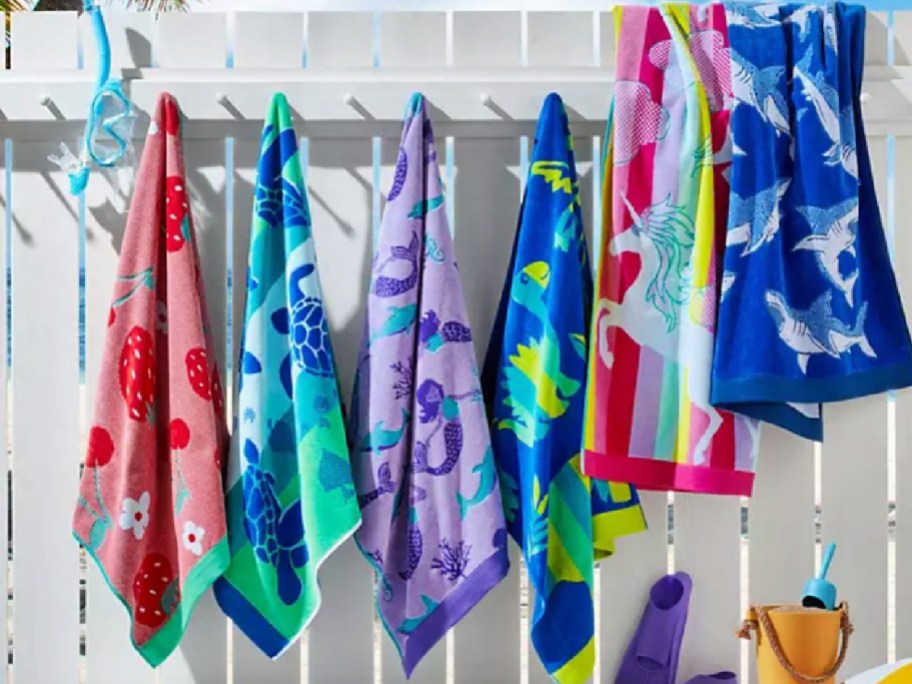 Colorful kids, beach towels hanging off white pegs on wooden fence