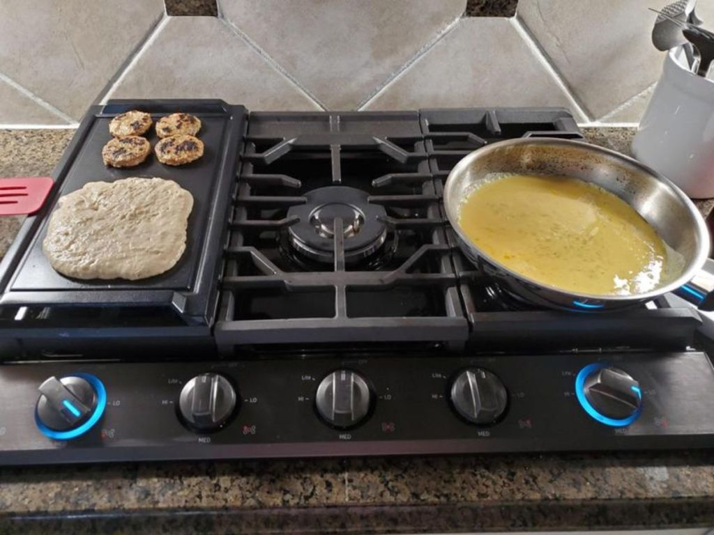 Samsung gas cooktop being used to make breakfast including a griddle with pancakes and a sautee pan of eggs