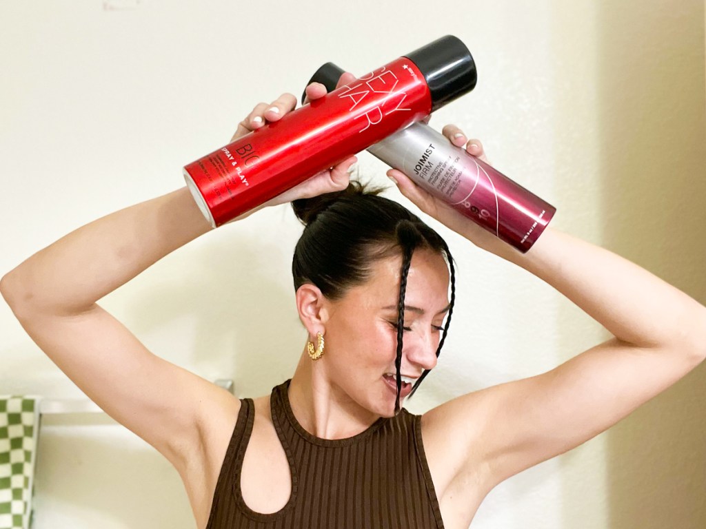 woman holding 2 cans of hair spray above her head