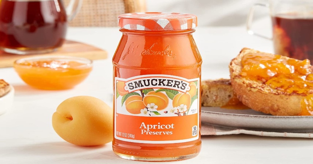Jar of Smucker's Apricot Preserves on a counter with fruit and cup of tea and toast in the background