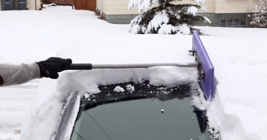 person using snow broom to clean snow off a car
