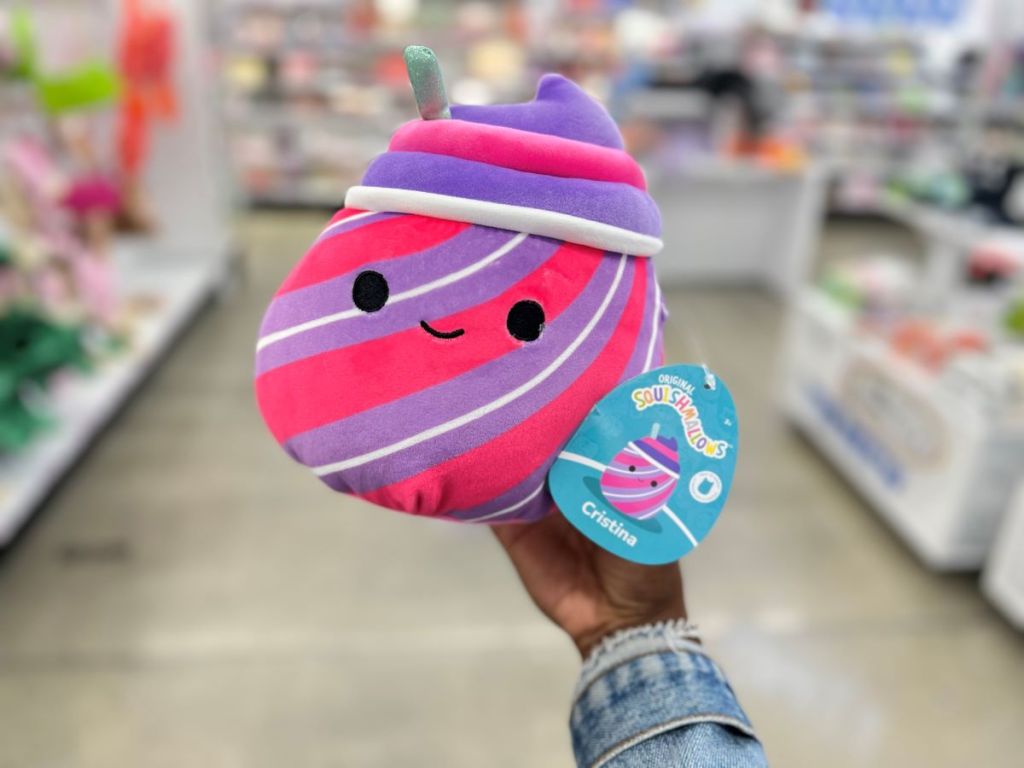 Hand holding a Squishmallow that looks like a purple, white, and pink striped slushie