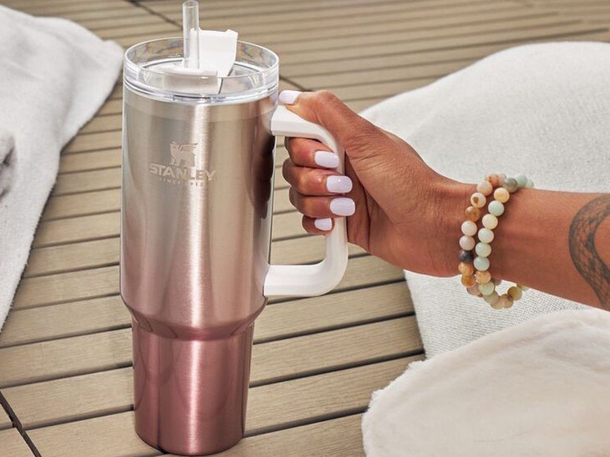 Woman's hand reaching for a rose gold stanley Quencher tumbler